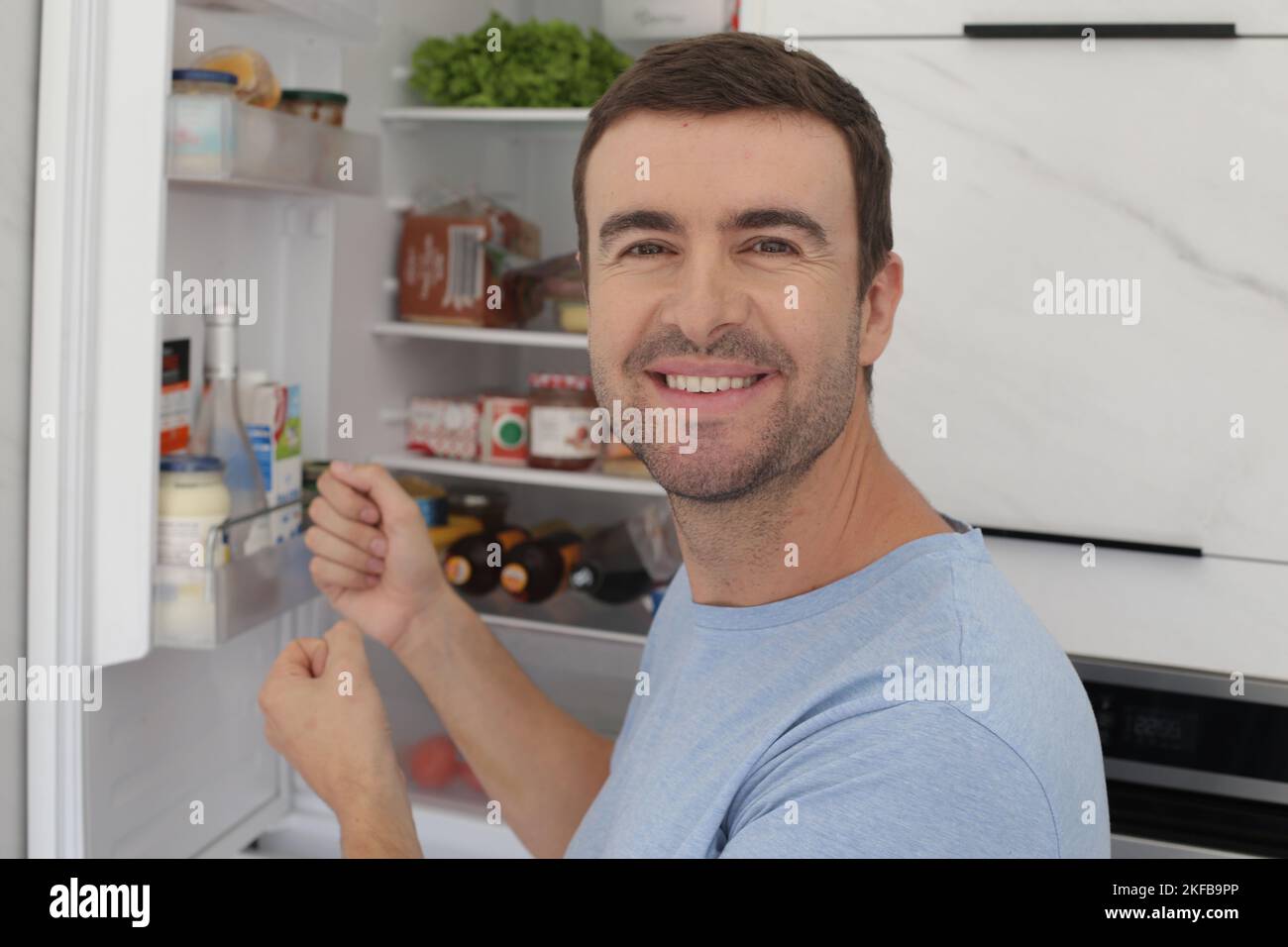 Lächelnder Mann mit offenem Kühlschrank im Hintergrund Stockfoto