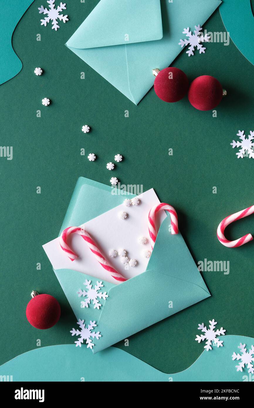 Schreiben von Weihnachtsgrüßen - Federkiel und Grußkarten in Papierumschlägen. Weihnachten Hintergrund mit Süßigkeiten Stöcke, magentafarbene Schmuckstücke, Schneeflocken. Draufsicht Stockfoto