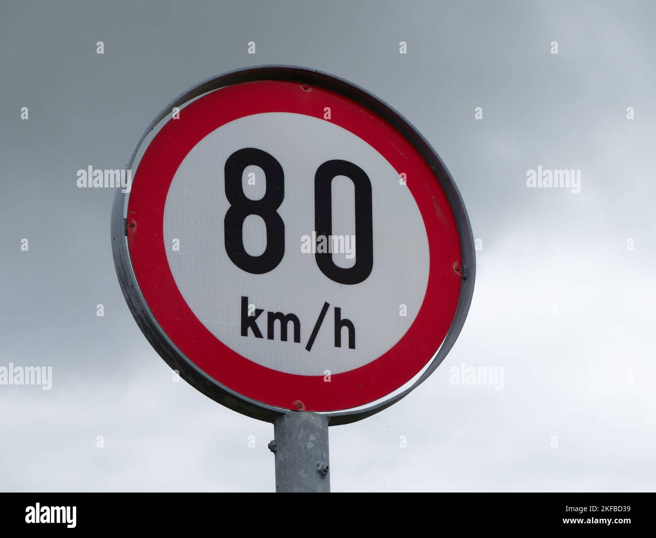 Rundes Straßenschild, das die Geschwindigkeit auf dem Hintergrund eines bewölkten Himmels begrenzt. Schilder, die auf eine Höchstgeschwindigkeit von 80 km h hinweisen Stockfoto