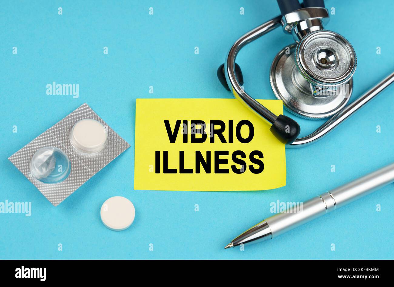 Medizinisches Konzept. Auf einer blauen Oberfläche, einem Stethoskop, Pillen, einem Stift und einem gelben Aufkleber mit der Aufschrift - Vibrio Krankheit Stockfoto