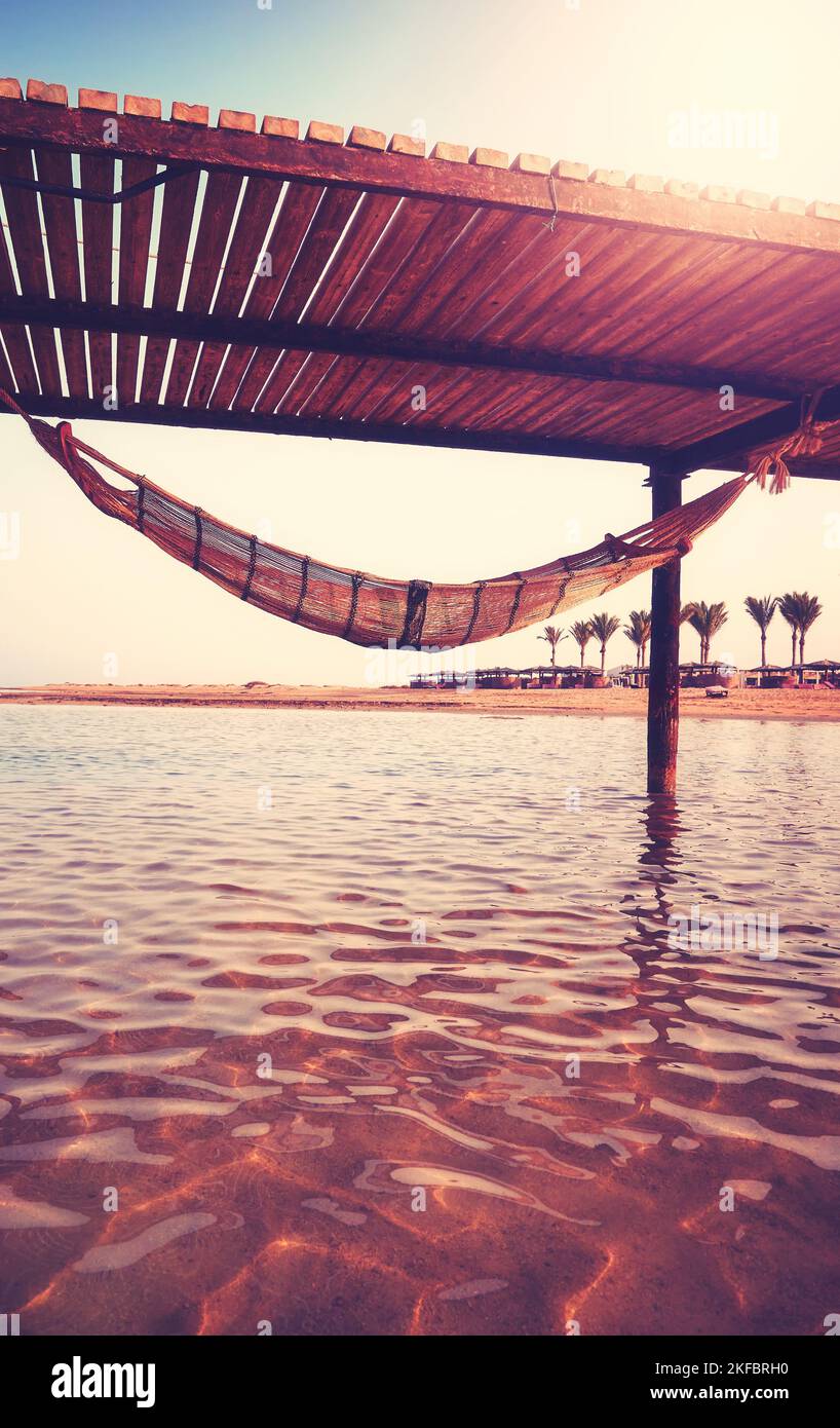 Leere Hängematte, die unter einem hölzernen Seebrücke am Meer hängt, Fluchtweg-Konzept, Farbtonierung angewendet. Stockfoto