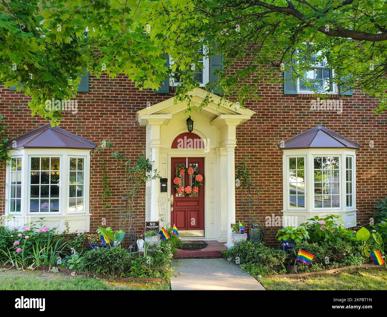 Hübsches traditionelles Haus mit Säulen auf der Veranda und Blumenkranz mit Landschaftsgestaltung und einem Baum und Stolz Fahnen Stockfoto