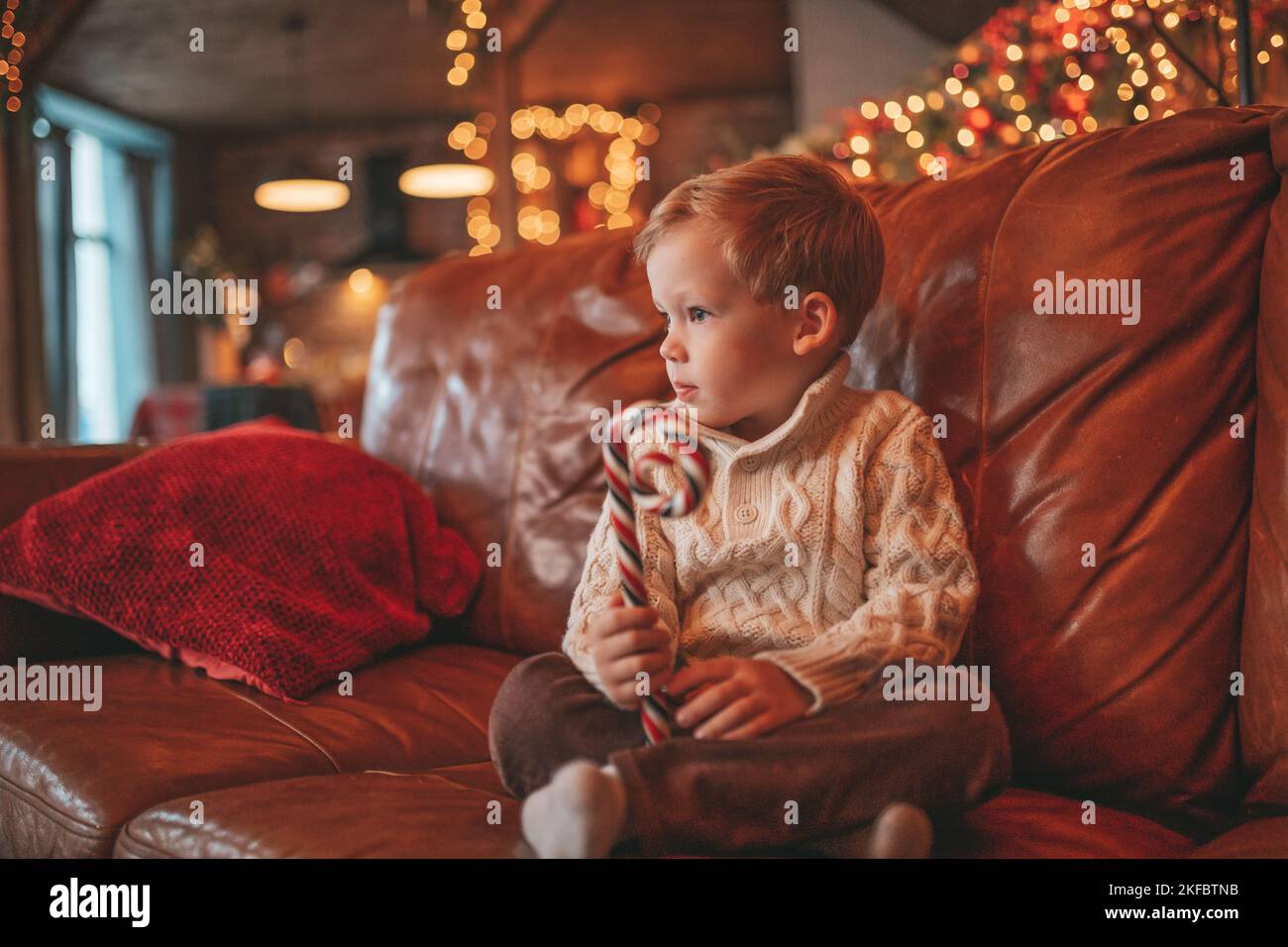 Happy Little boy Träumer wartet auf Wunder Santa genießen Süßigkeiten Farbe Lollipop. Fröhliches Kind in Strickmode Outfit feiern Neujahr halten Weihnachten Tasse mit Stockfoto