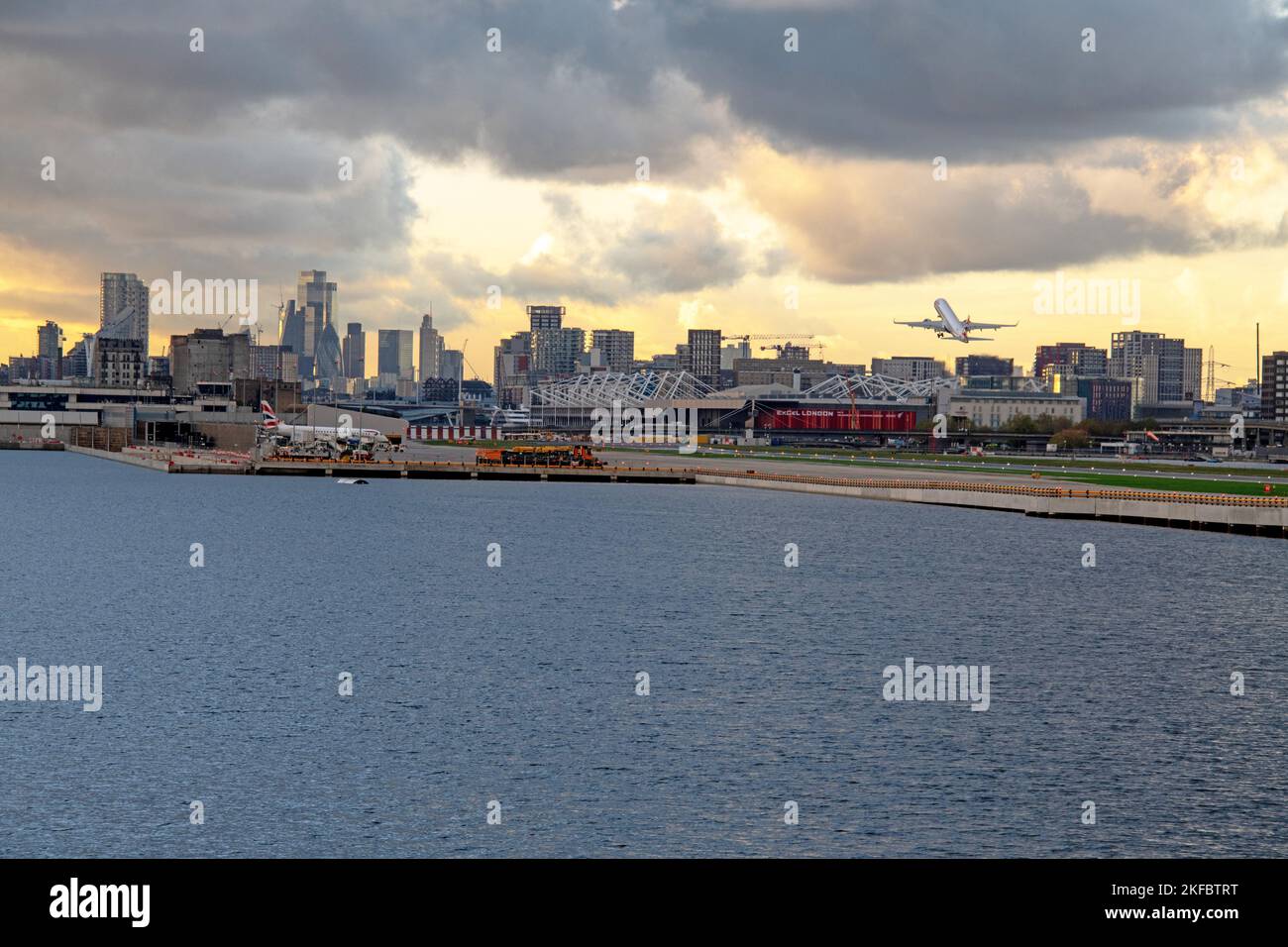 Ein Embraer ERJ-190 von British Airways hebt sich am Flughafen London City mit Canary Wharf im Hintergrund in dunkle Wolken ab. Stockfoto