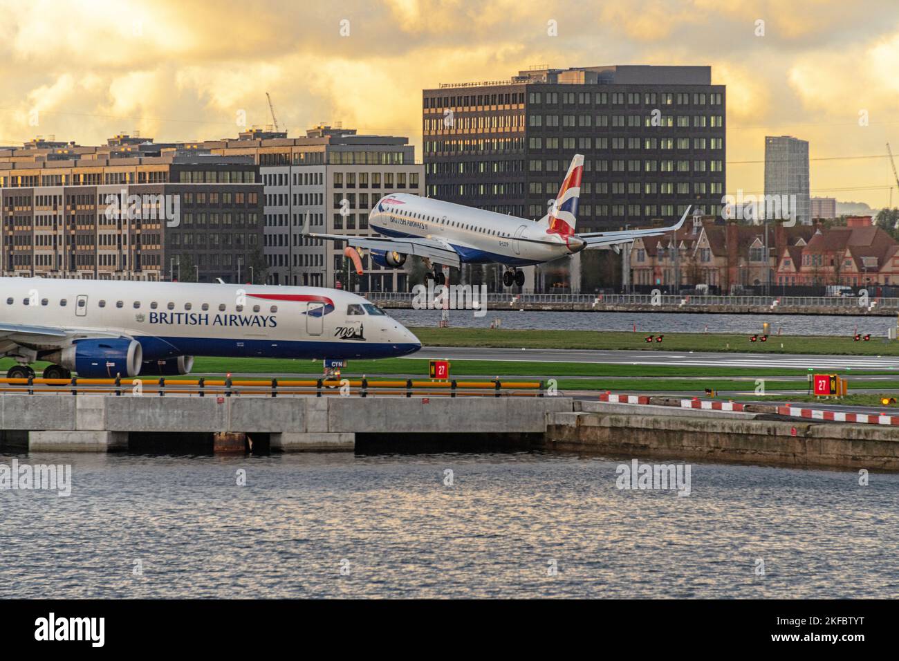 Ein Embraer ERJ-190 von British Airways hebt sich am Flughafen London City in dunkle Wolken ab, während ein weiteres Taxi entlang der Start- und Landebahn fährt. Stockfoto