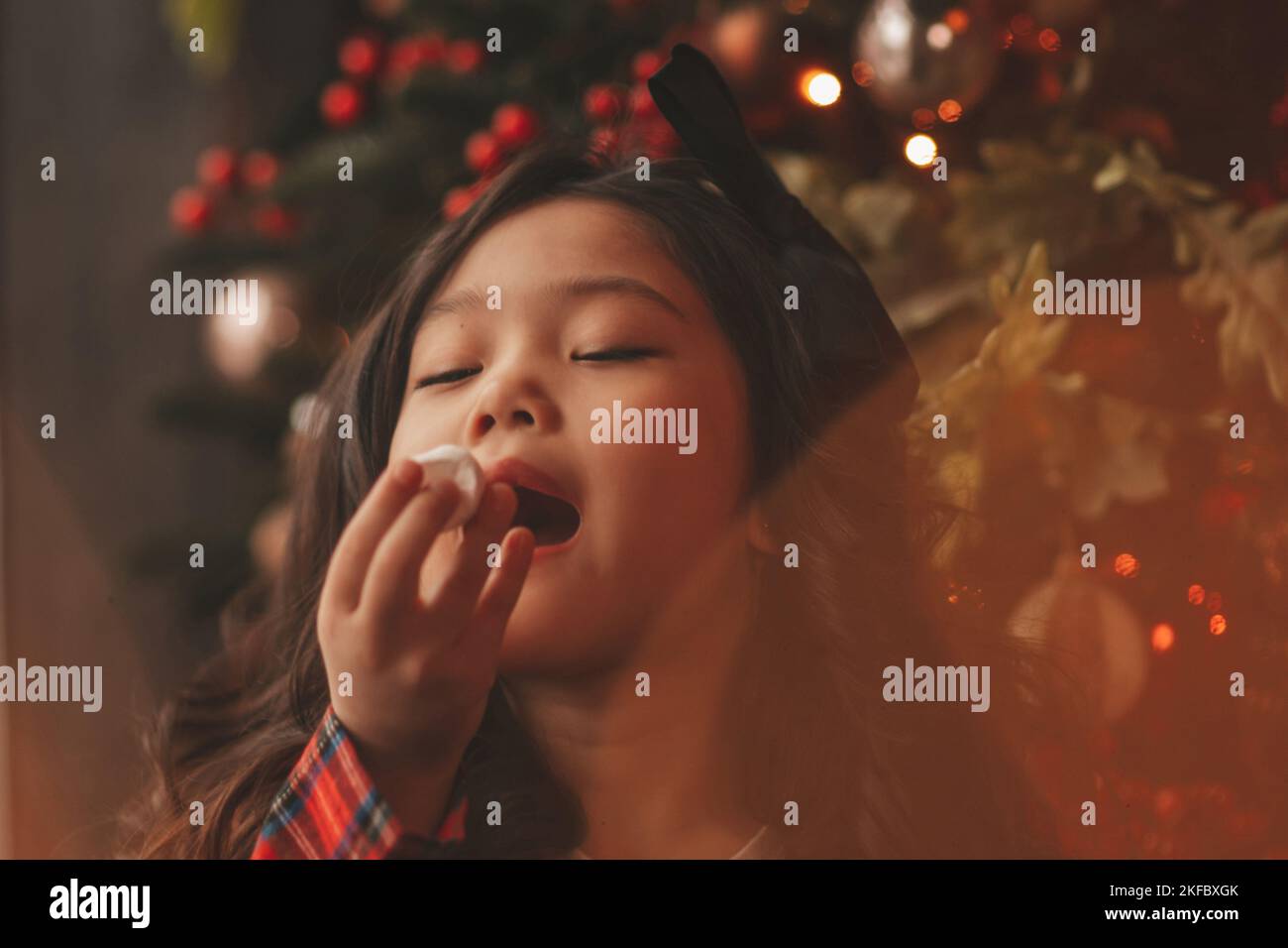 Happy japan kleines Mädchen Träumer warten Wunder Santa genießen Süßigkeiten in der Nähe von noel Baum. Asiatische Kind in rot kariert Outfit feiert Neujahr halten Xmas Cup wi Stockfoto