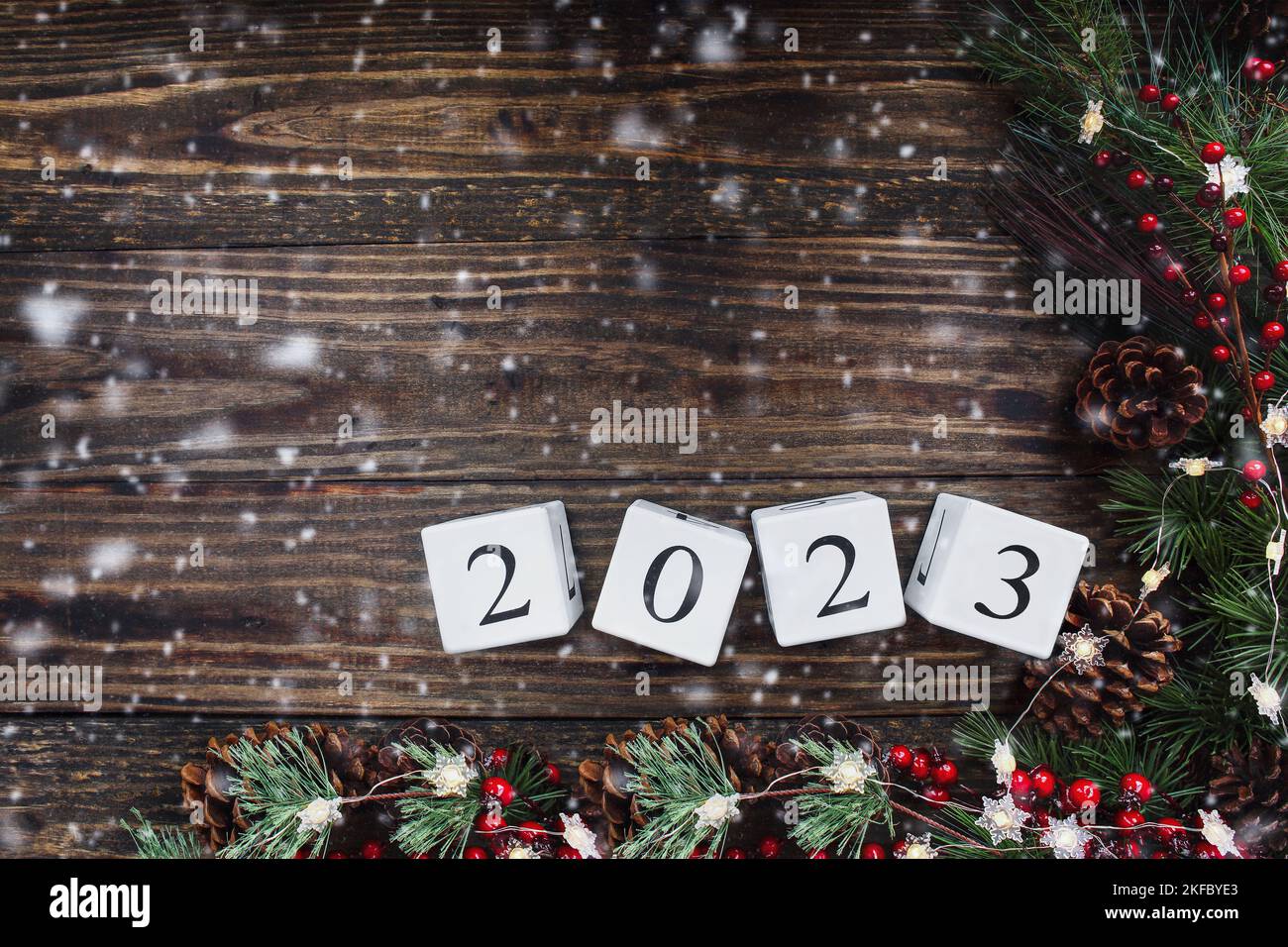 Silvester 2023 Holzkalenderblöcke. Weihnachtsbaumbeleuchtung, Kiefernäste, rote Winterbeeren und Schnee auf Holztisch-Hintergrund. Draufsicht. Stockfoto