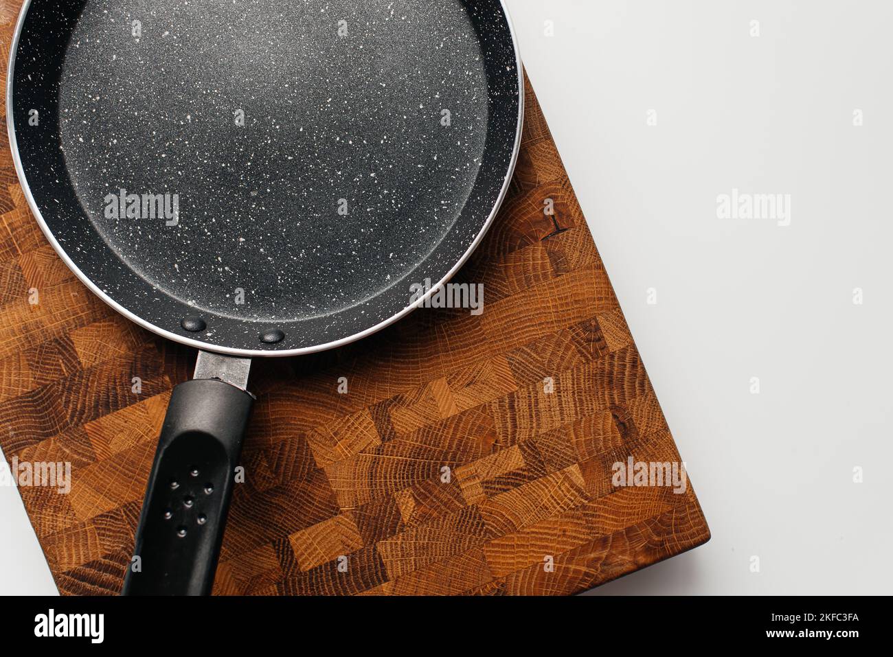 Leere Pfanne auf Holzbrett. Leerer, mit Marmor beschichteter Eisentopf Stockfoto