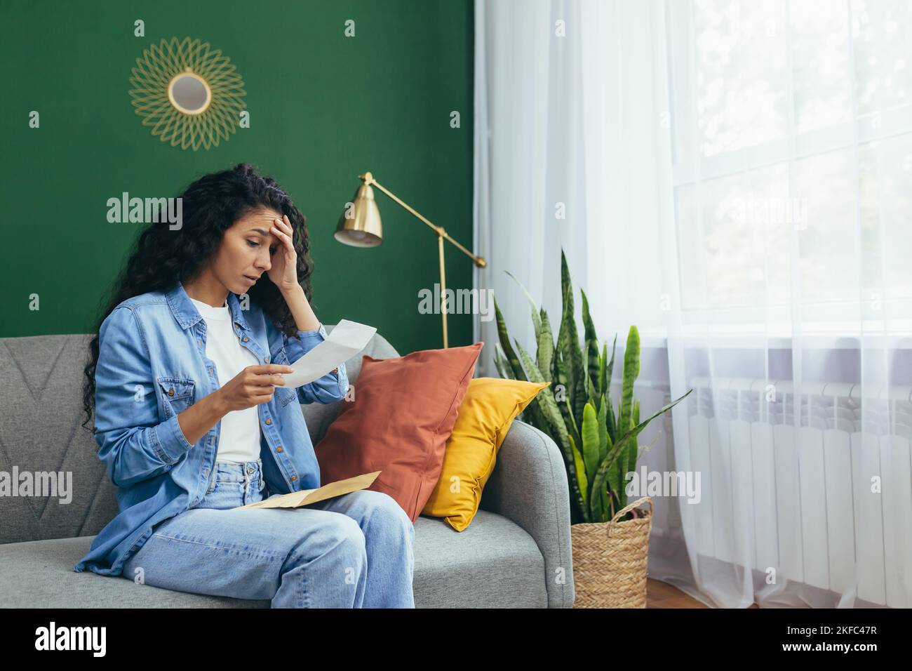 Eine junge lateinamerikanische Frau erhielt Scheidungspapiere. Zu Hause auf dem Teppich sitzend, ein Blatt Papier in den Händen haltend, schockiert, ihren Kopf haltend. Stockfoto