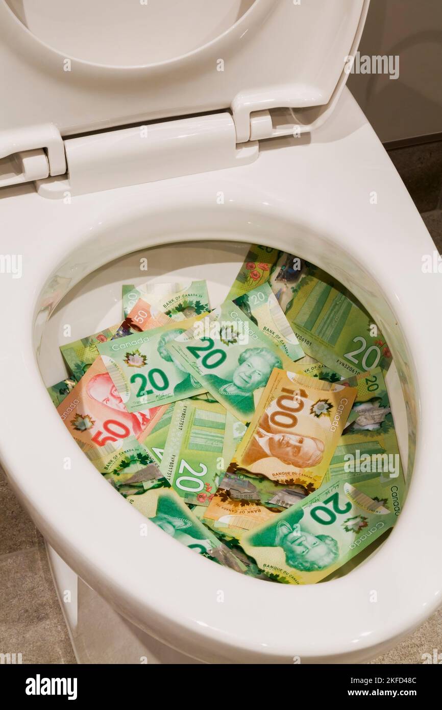 Kanadische zwanzig-, fünfzig- und einhundert-Dollar-Scheine in einer weißen Toilettenschüssel aus Porzellan. Stockfoto