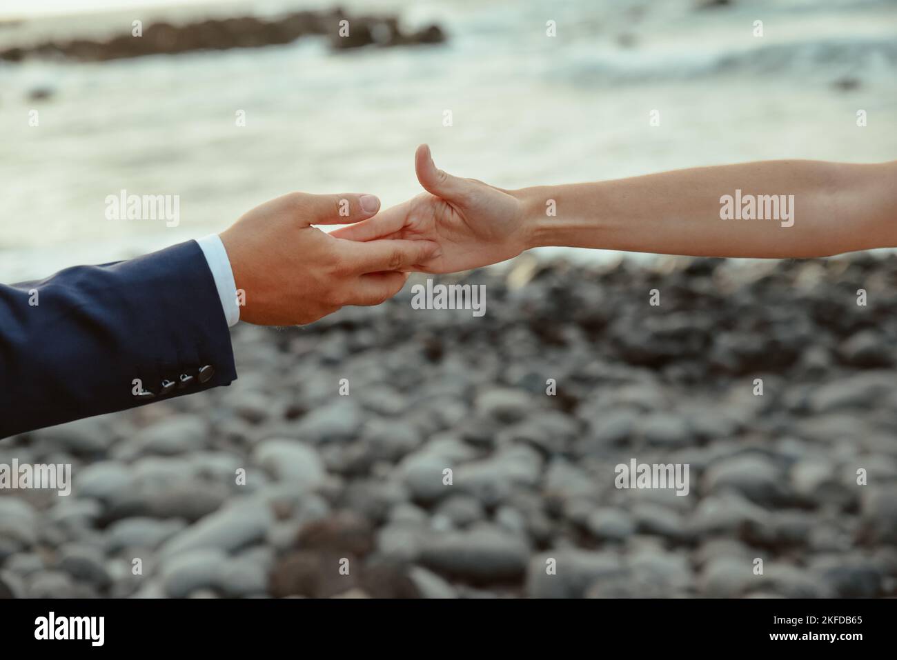 Eine Nahaufnahme eines Mannes und einer Frau, die die Hände an einem felsigen Strand berühren - Liebeskonzept Stockfoto