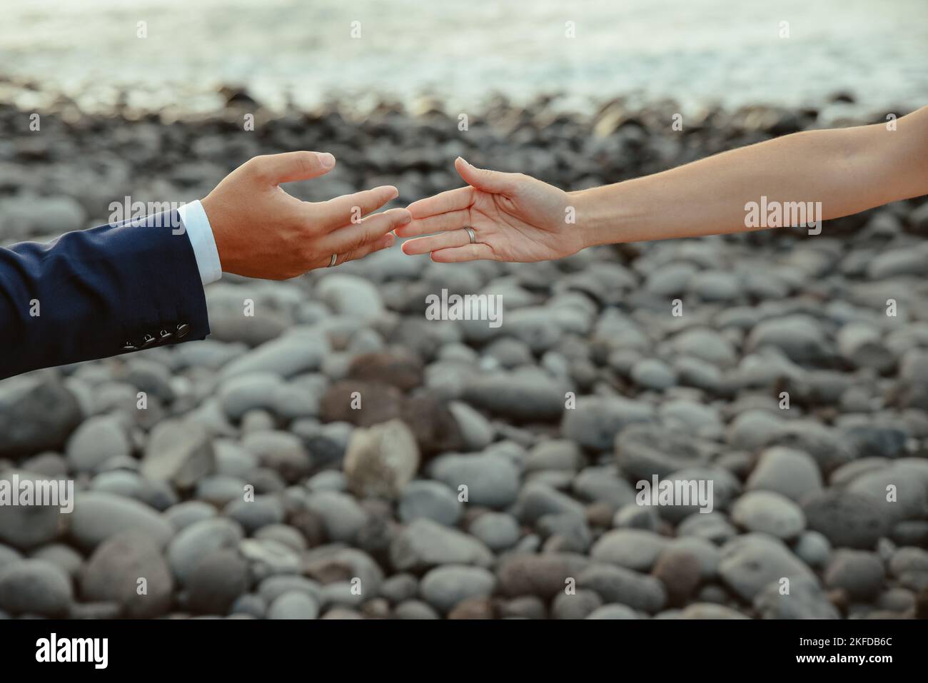 Eine Nahaufnahme eines Mannes und einer Frau, die die Hände an einem felsigen Strand berühren - Liebeskonzept Stockfoto