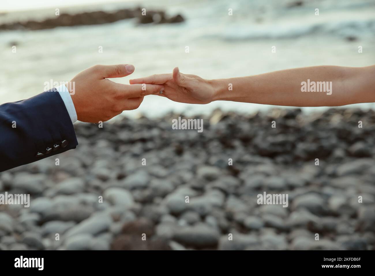 Eine Nahaufnahme eines Mannes und einer Frau, die Hände an einem felsigen Strand halten - Liebeskonzept Stockfoto