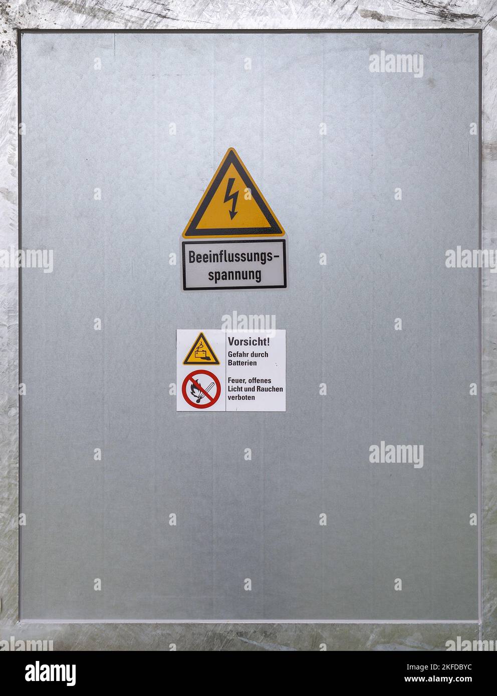 Eine Metalltür mit deutschen Warnschildern gegen elektrische Hochspannung - „Einflussspannung“ Stockfoto