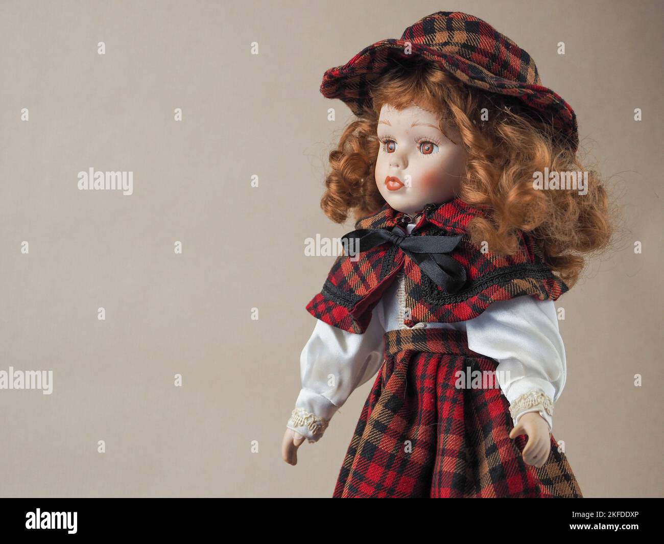 Vintage Porzellan Puppe Mädchen mit braunen Augen mit rot fließenden  lockigen Haaren in einem karierten schwarz und rot Kleid und Hut.  Porzellanpuppen erschienen im 18.. Jahrhundert in Frankreich. Sie wurden  verwendet, um