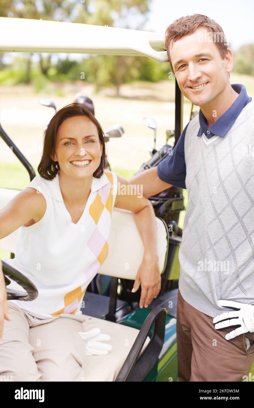 Ihre Liebe zum Golf brachte sie zusammen. Lächelnde Frau, die in einem Golfwagen saß und ihren Mann neben ihr stand. Stockfoto