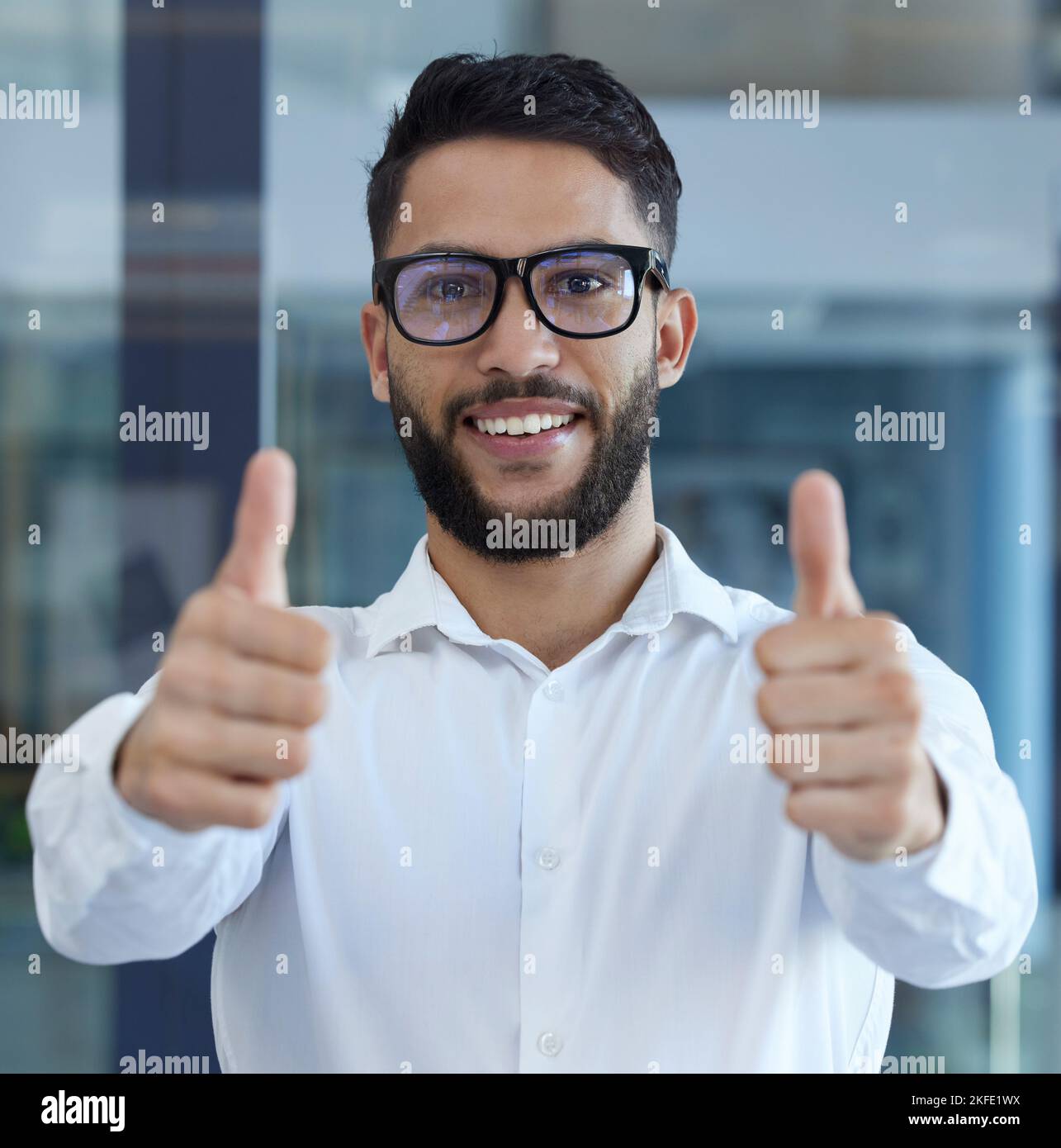 Portrait, Daumen hoch und vielen Dank mit einem Geschäftsmann, der in seinem Büro als Gewinner steht und Ja sagt. Porträt, Vertrauen und Erfolg mit einem männlichen Mitarbeiter Stockfoto