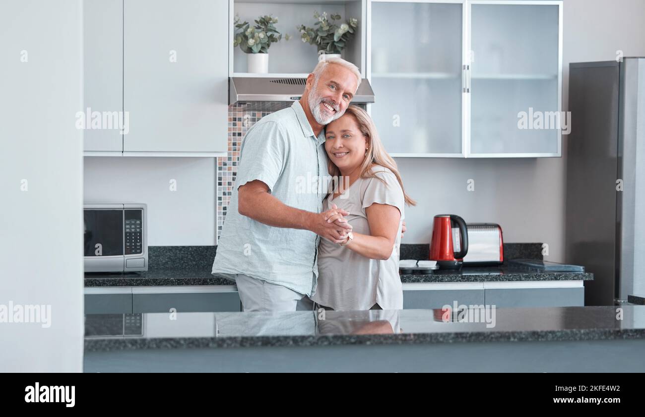 Liebe, Ehe und Tanz mit einem älteren Paar in der Küche ihres Hauses zusammen für die Bindung oder Romantik. Porträt, glücklich und lächeln mit einem reifen Stockfoto