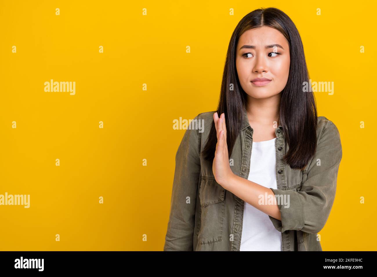 Porträt von traurig verärgert ernsthafte Frau mit langen Frisur tragen khaki Hemd suchen leeren Raum halten Handfläche isoliert auf gelbem Hintergrund Stockfoto