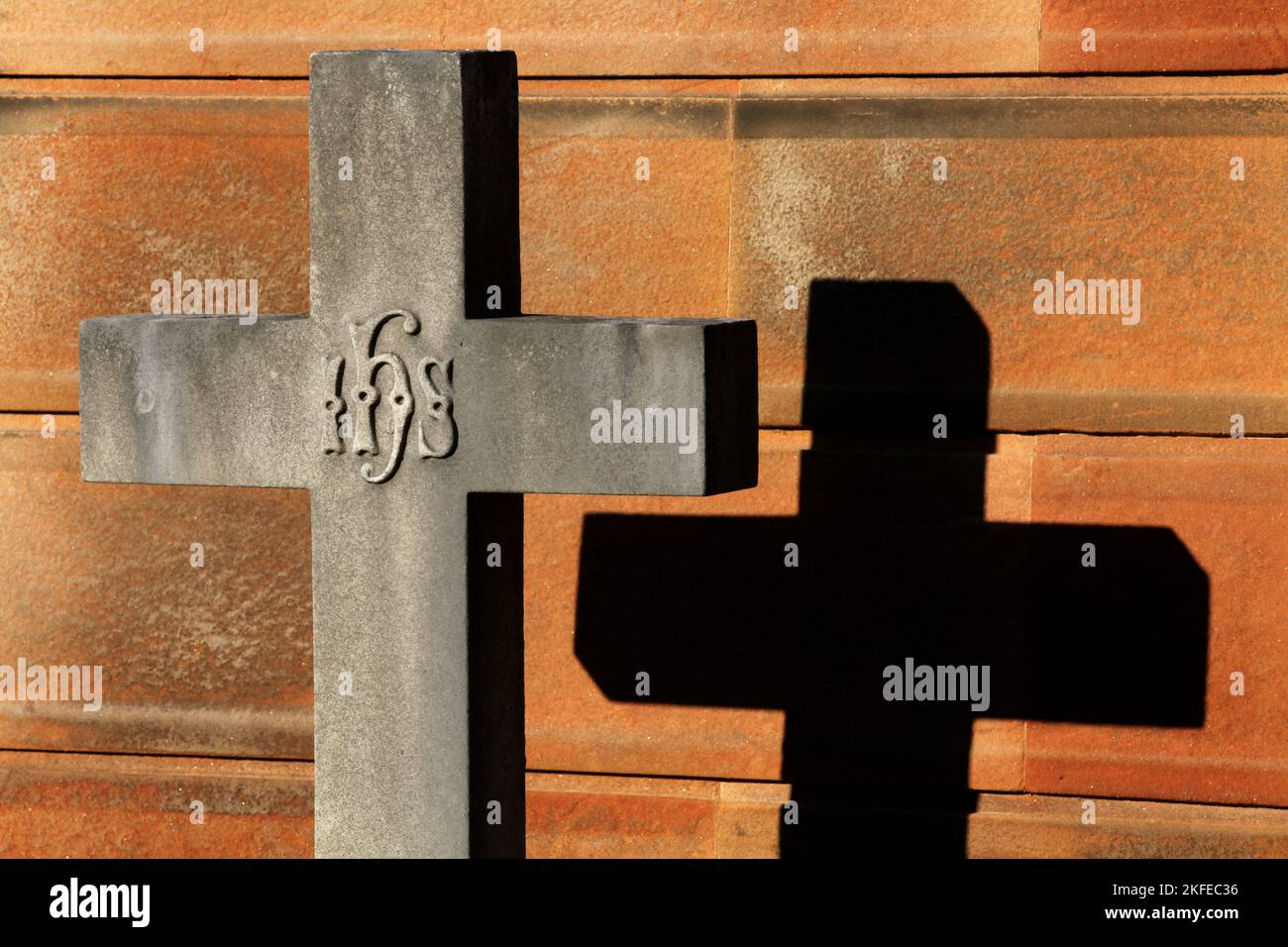 Ein Grabsteinkreuz mit seinem Schatten gegen die Wand dahinter Stockfoto