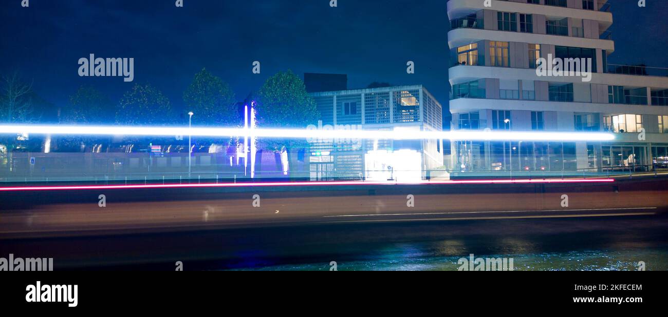 Lichtwege eines Bootes, das nachts durch eine Stadt mit einigen Gebäuden im Hintergrund führt Stockfoto