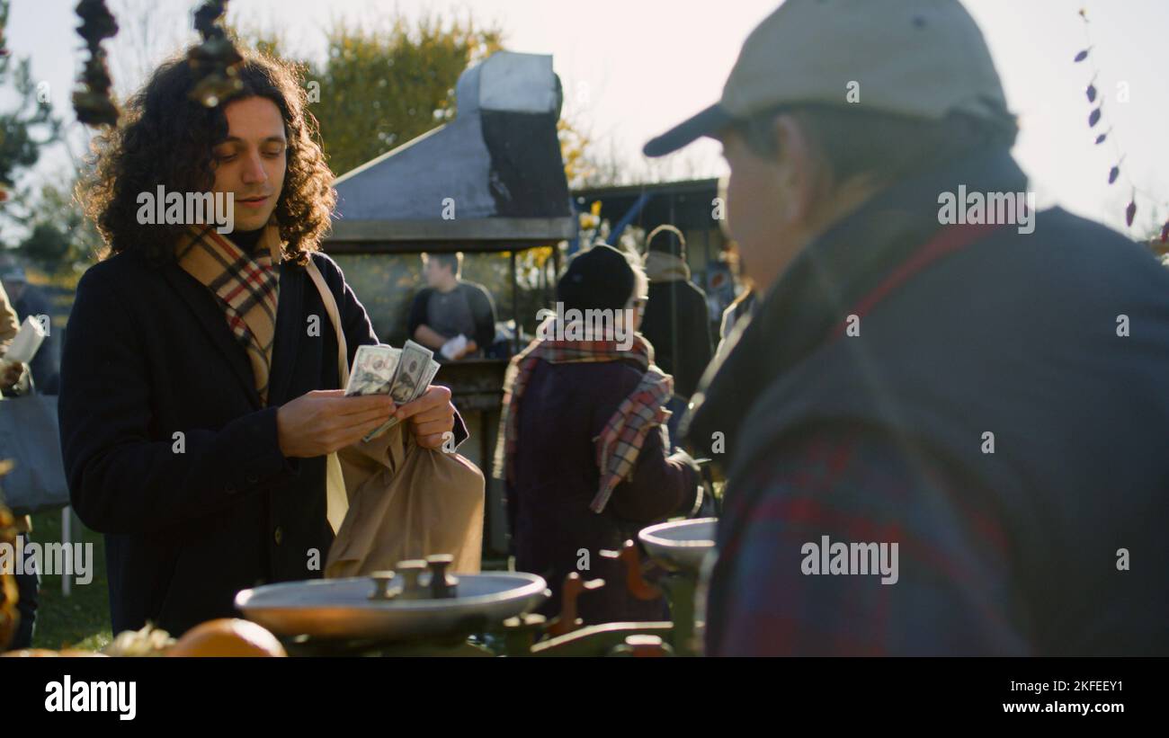 Senior Farmer gibt Öko-Tasche mit Waren an den Menschen. Er bezahlt kontaktlos Einkäufe per Smartphone. Wochenendeinkäufe auf dem lokalen Bauernmarkt im Freien. Vegetarische und Bio-Lebensmittel. Landwirtschaft. Stockfoto