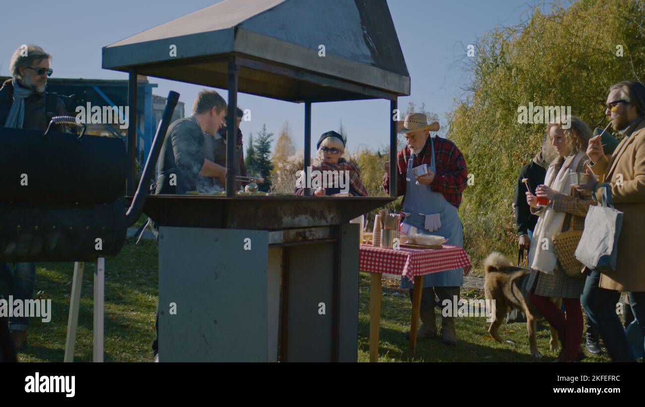 Menschen versuchen, Fleisch oder Gemüse auf dem Grill gekocht. Der Erwachsene Mann hebt bereit zum Essen ab und legt eine Portion auf den Teller. Wochenende auf dem lokalen Bauernmarkt. Stockfoto