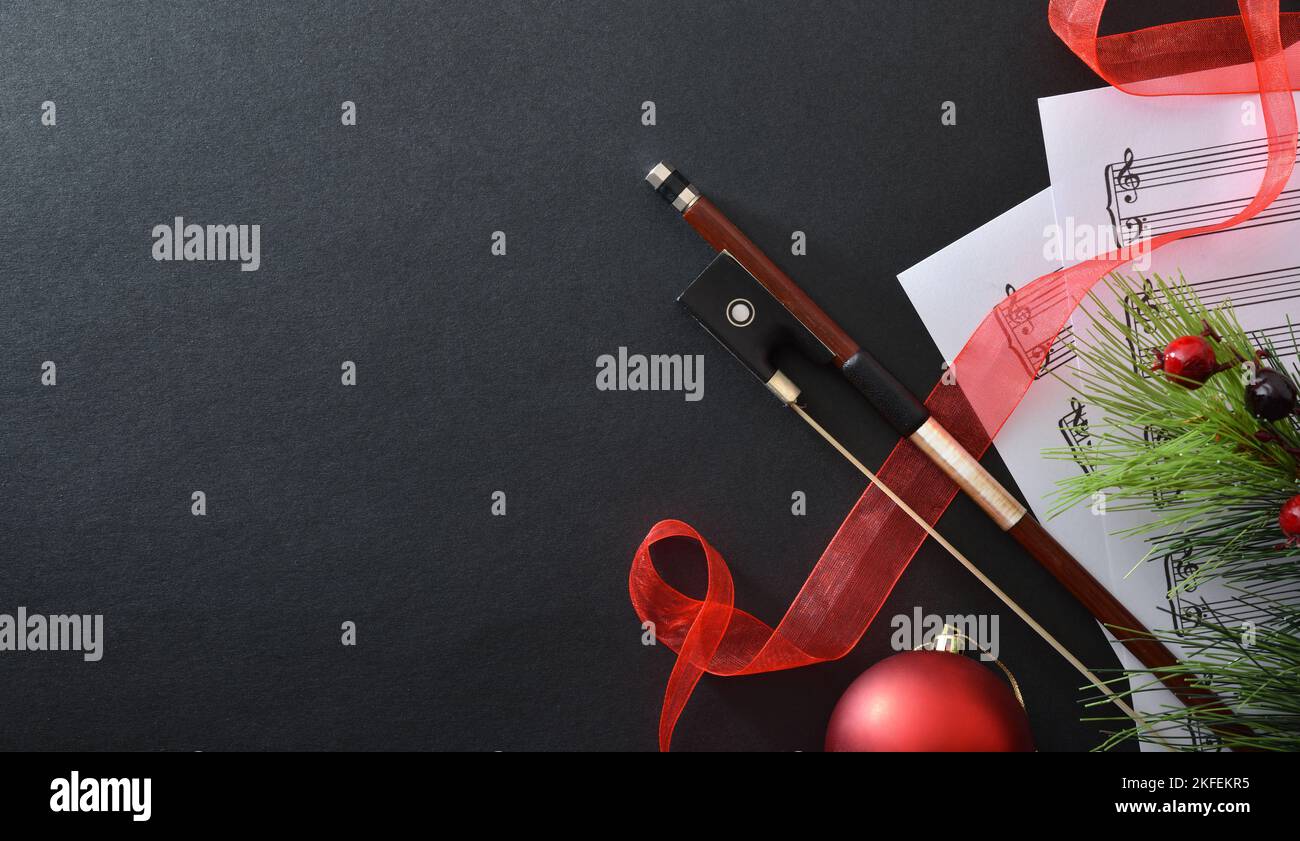 Konzept der Aufführung von Saiteninstrumenten mit Bogen auf Notenblättern mit weihnachtlicher Dekoration auf schwarzem Hintergrund. Draufsicht. Stockfoto
