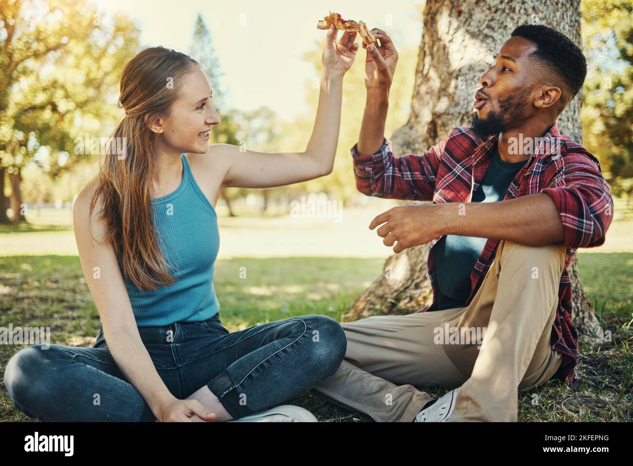 Entspannen Sie sich, Pizza und glücklich mit Paar im Park für Picknick, Fast Food und Sommertermin. Liebe, Jugend und Freiheit mit schwarzen Männern und Frauen beim Mittagessen Stockfoto