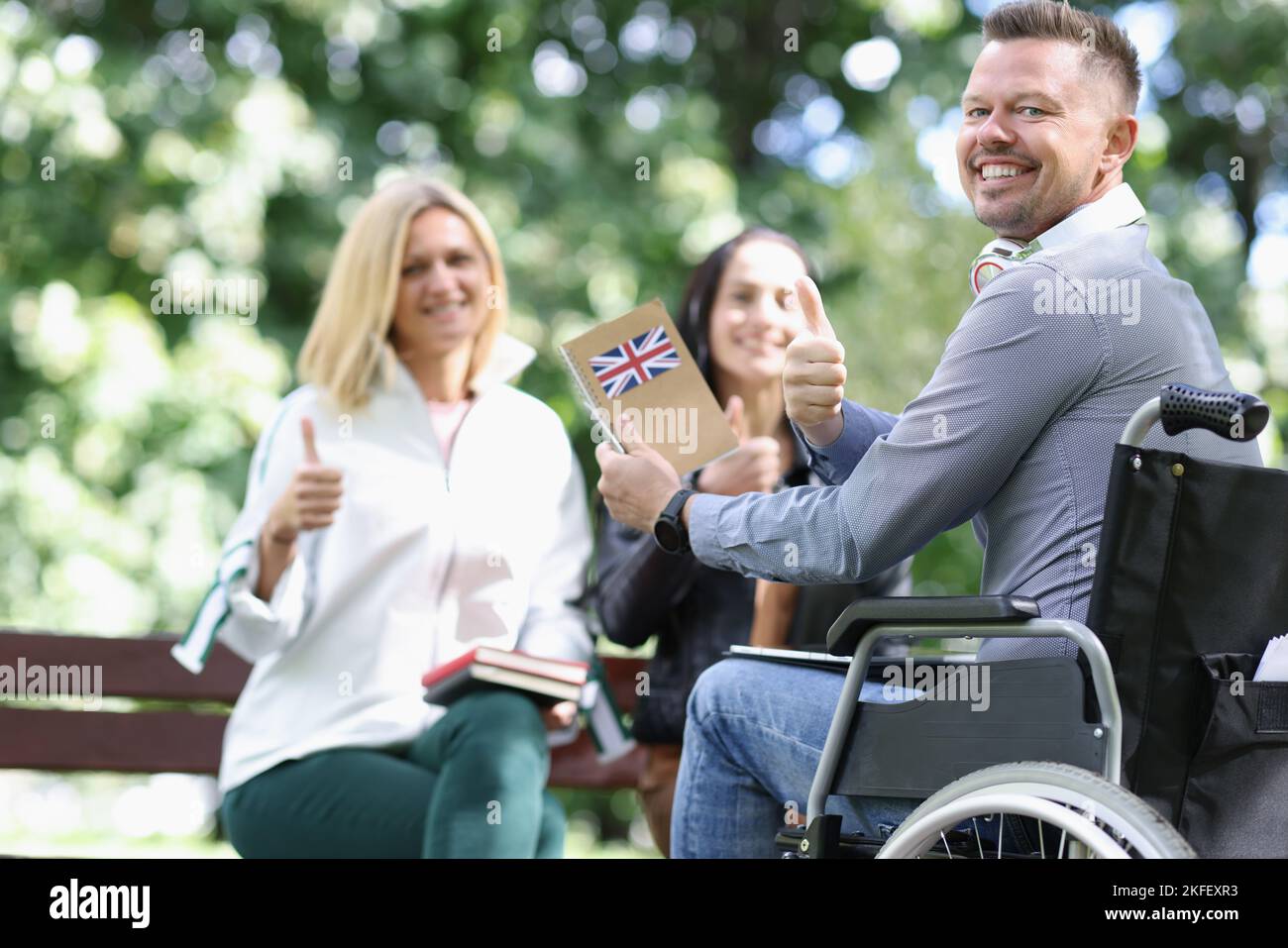 Glücklicher behinderter Mann im Rollstuhl lernt mit seinen Freunden Englisch. Stockfoto