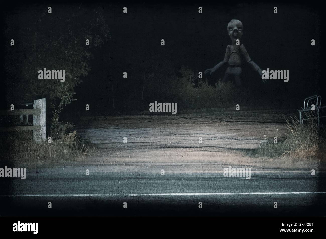 Eine riesige Horrorpuppe. Nachts durch Autoscheinwerfer auf dem Land beleuchtet. Mit einer gruseligen Found Footage-Bearbeitung. Stockfoto