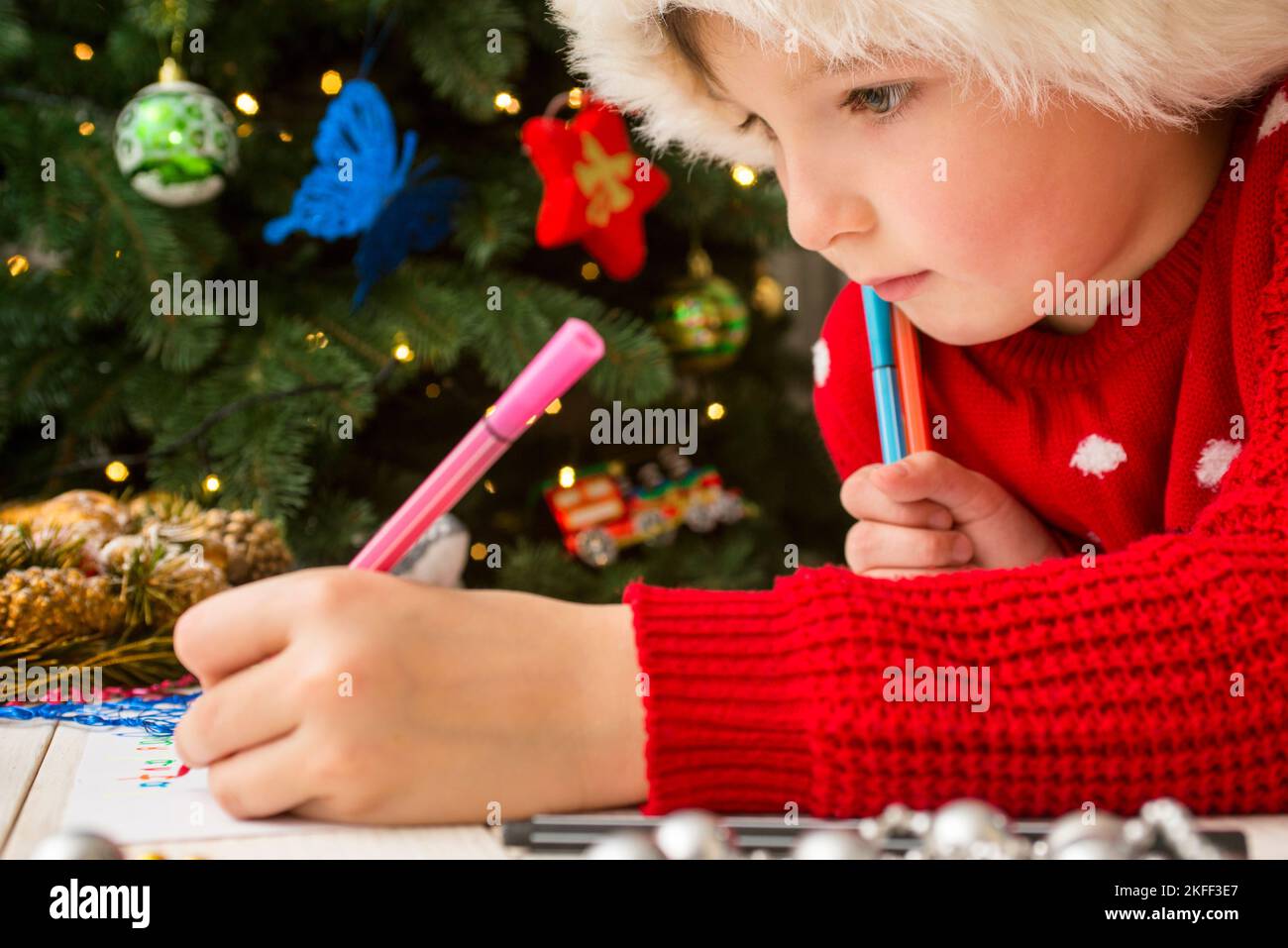 Kleiner Junge in Weihnachtsmütze schreibt Brief an den Weihnachtsmann Stockfoto