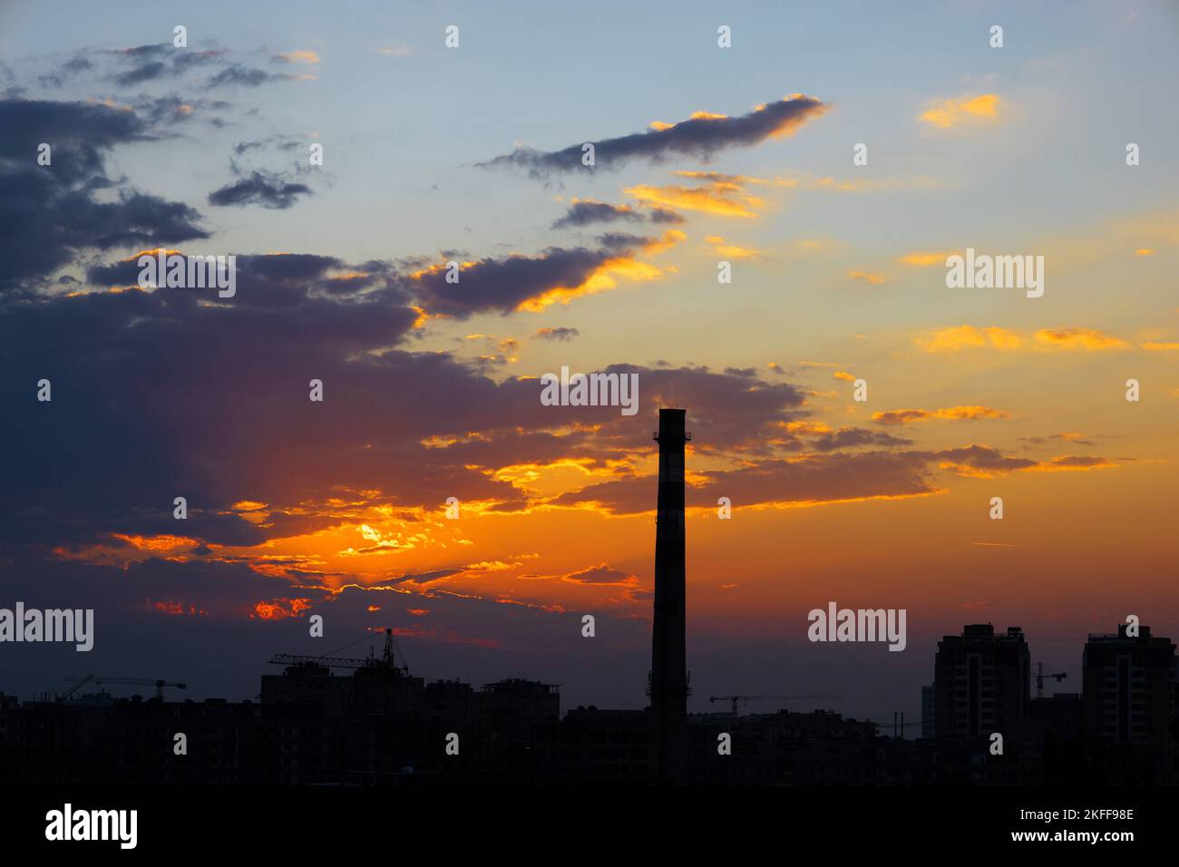 Umriss eines hohen Schornsteinturms und von Gebäuden während des Sonnenuntergangs mit dramatischen Wolken und Farben. Stockfoto