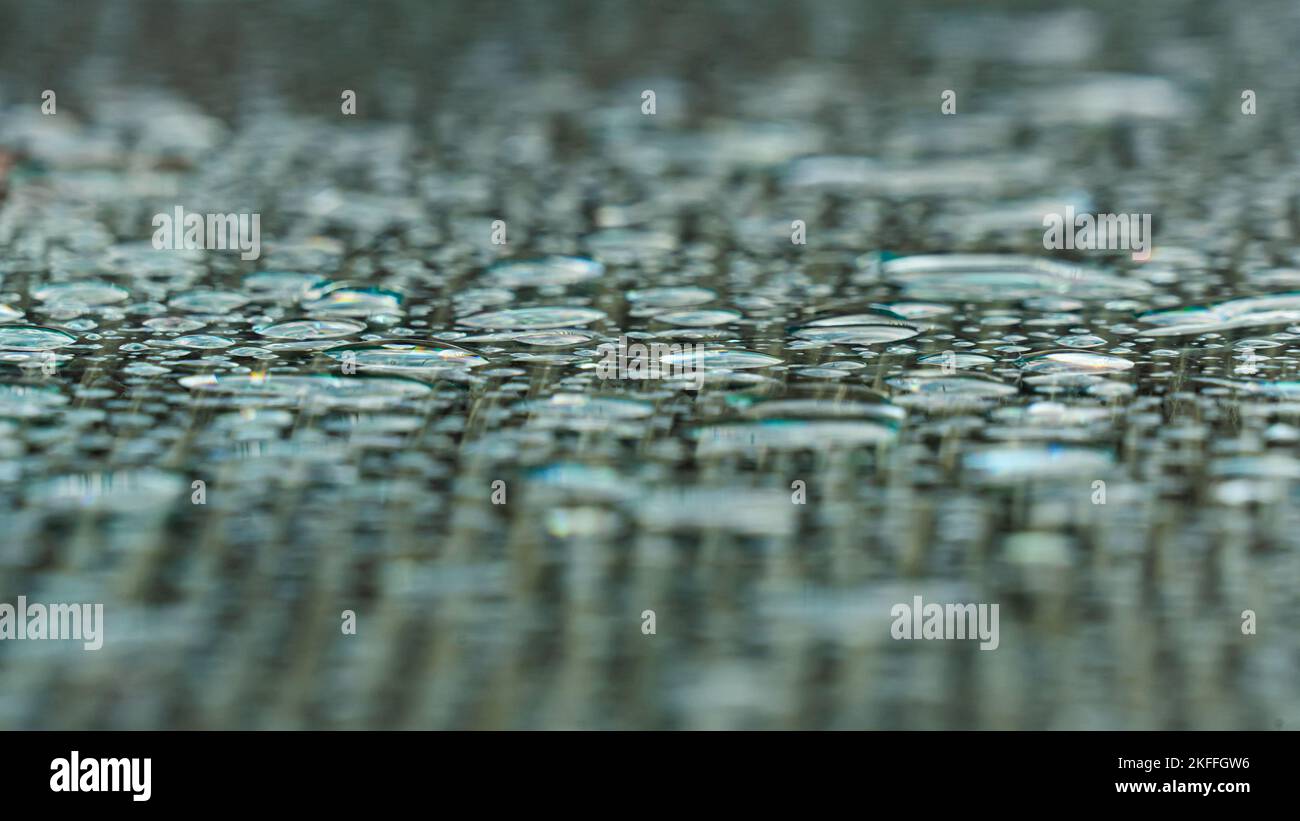 Regentropfen auf der Glasoberfläche eines Gartentisches bilden ein monochromatisches Muster Stockfoto
