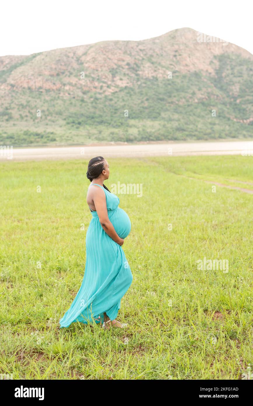 Eine schwangere Mutter, die ihren wachsenden, schwangeren Bauch hält und die Vorfreude auf die Geburt ihres Babys genießt Stockfoto