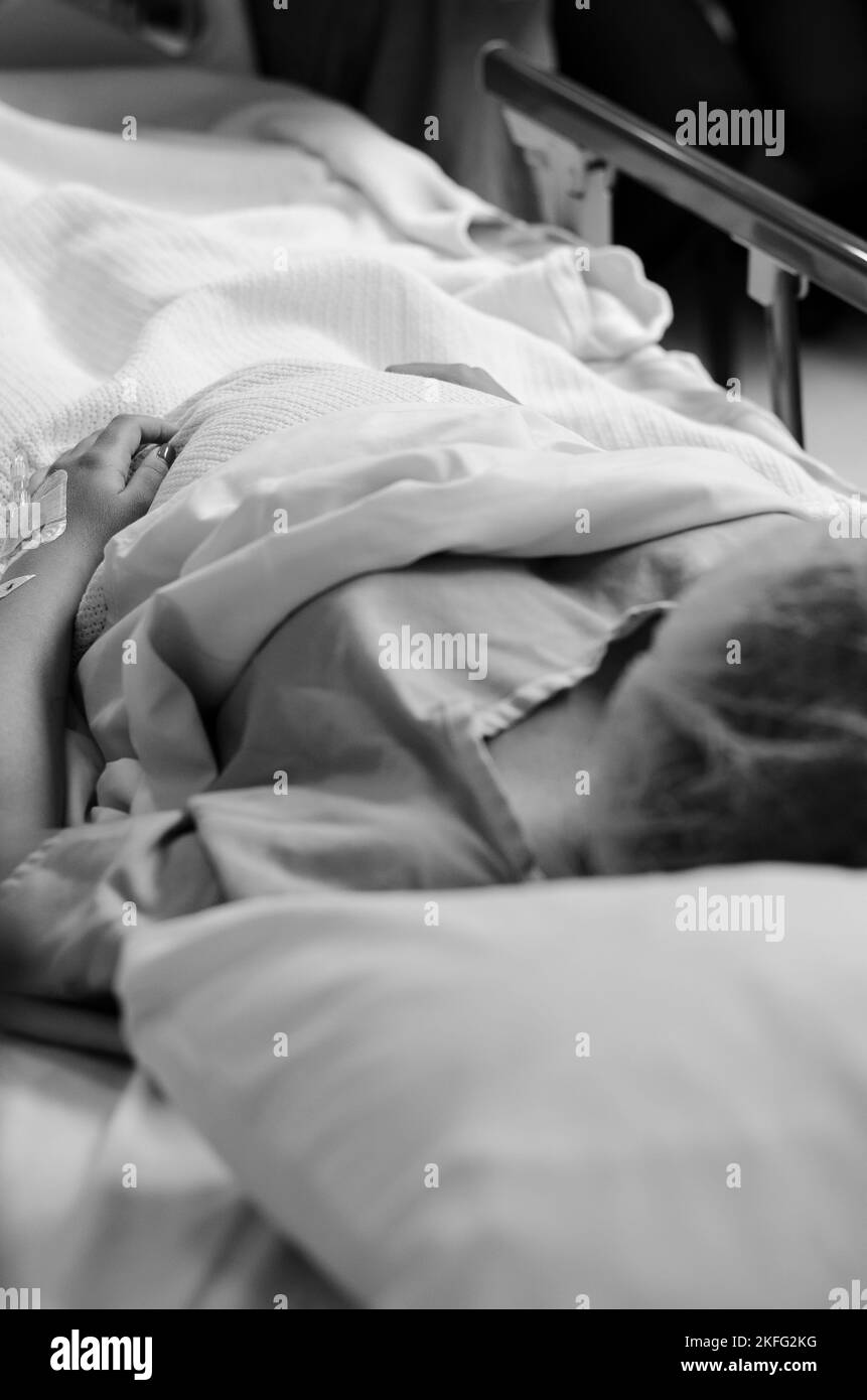 Eine schwangere Frau in den Wehen, die in einem Krankenhausbett liegt und auf die Geburt ihres Babys wartet. Stockfoto