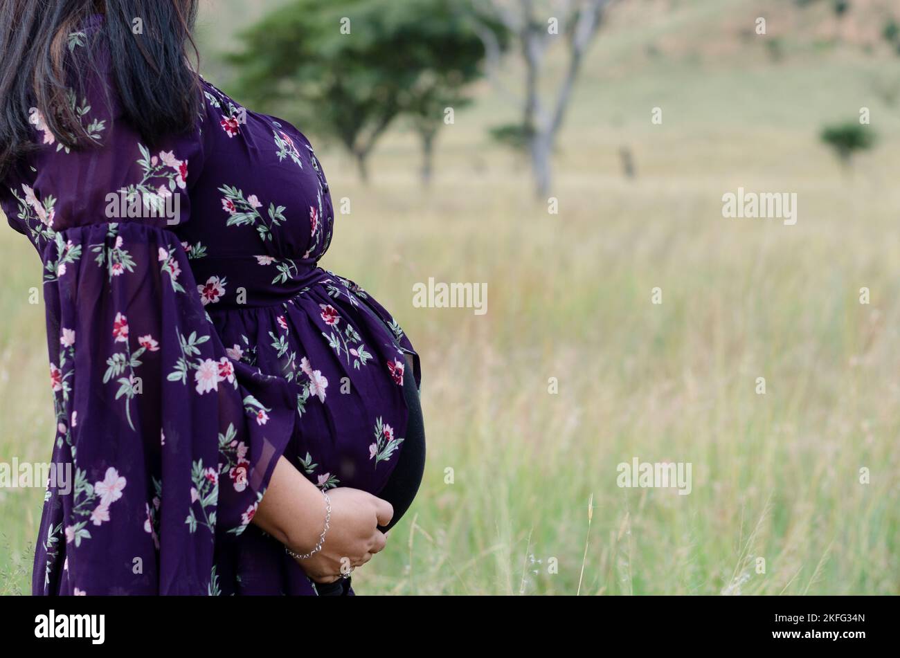 Eine schwangere Mutter, die ihren wachsenden, schwangeren Bauch hält und die Vorfreude auf die Geburt ihres Babys genießt Stockfoto
