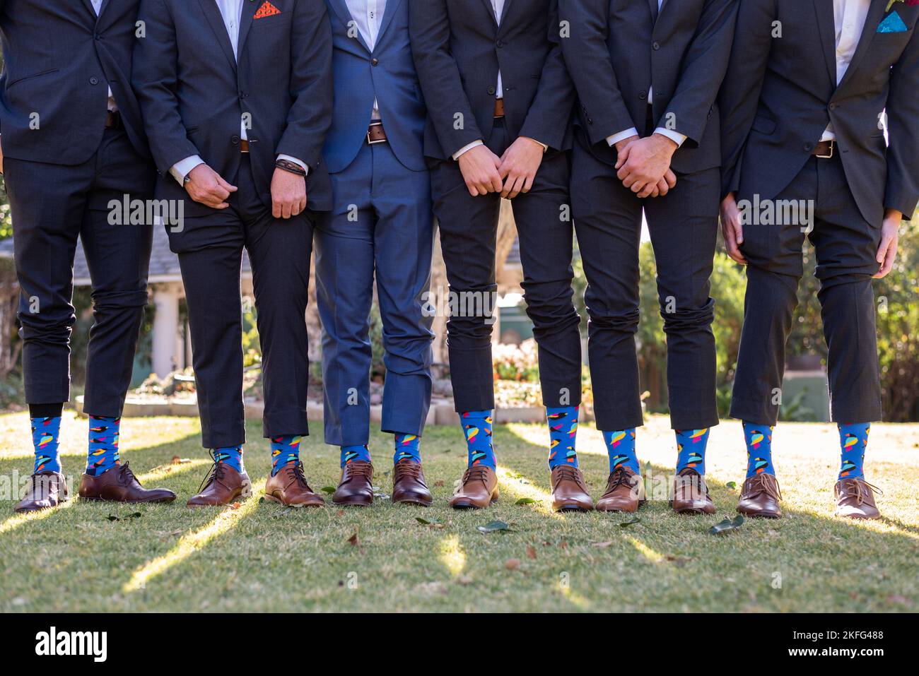 Männer stehen hintereinander mit angehobenen Hosen, um ihre Socken auf einer Hochzeit zu enthüllen Stockfoto
