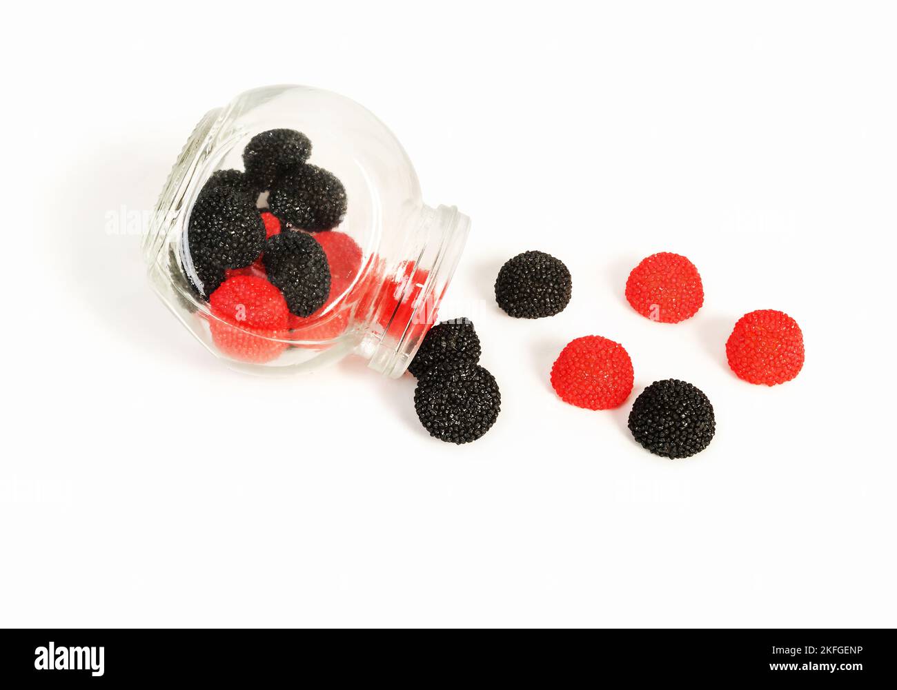Süße schwarze und rote Fruchtsaftgelees in Form von Brombeeren und Himbeeren, die aus einem Glas strömen. Stockfoto