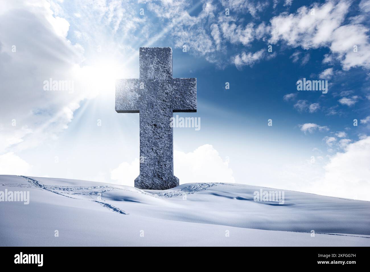 Großes christliches Steinkreuz in einer Berglandschaft mit Schnee vor einem klaren blauen Himmel mit Wolken, Sonnenstrahlen und Kopierraum. Stockfoto