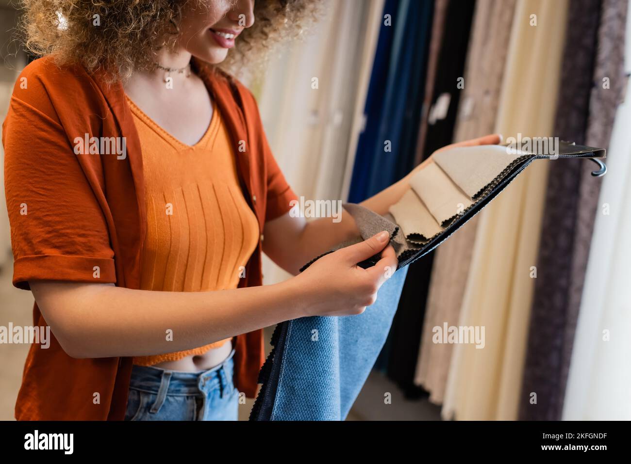 Beschnittene Ansicht einer jungen lockigen Frau, die im Textilgeschäft ein Stoffmuster berührt Stockfoto