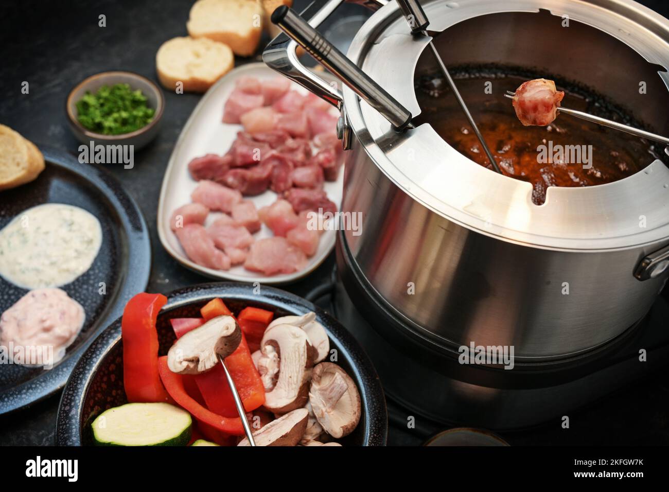 Deutsches Fondue mit rohem Fleisch und Gemüse, das auf langen Gabeln in einem Topf mit kochendem Öl gebraten wird, wird oft für Familie und Freunde an Feiertagen wie N serviert Stockfoto