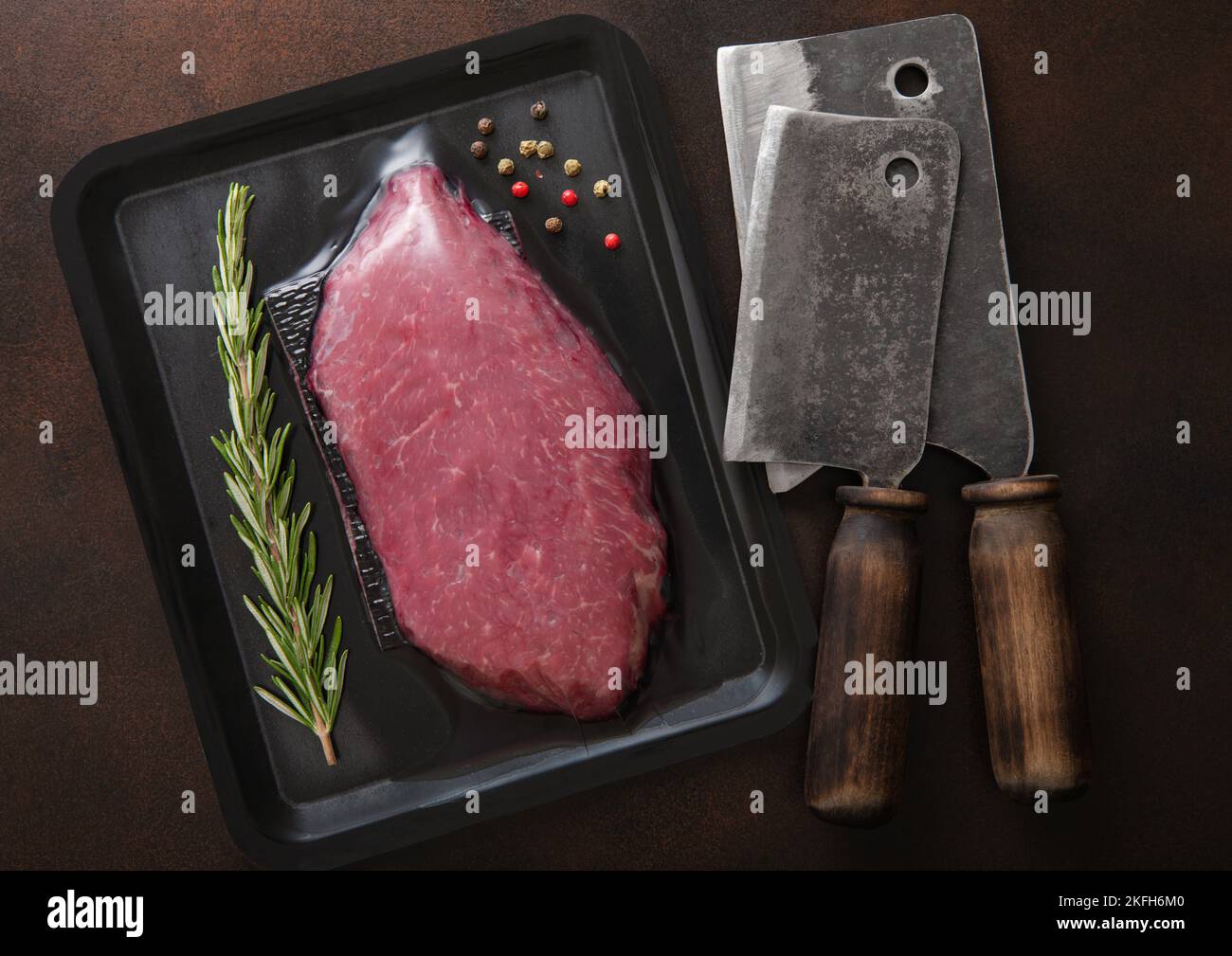 Rinderfiletsteak in Vakuumschale mit Fleischspalten auf dunklem Hintergrund mit Rosmarin und Pfeffer.Draufsicht. Stockfoto