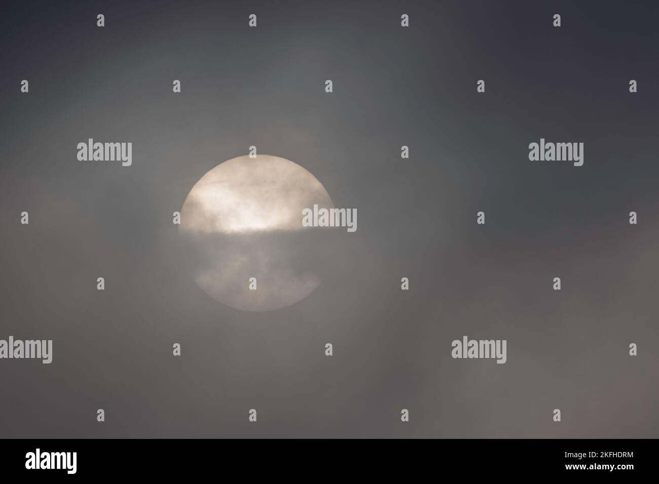 Früh morgens nebiger Sonnenaufgang. Die Sonne ist teilweise von dramatischen, stimmungsvollen Wolken verdeckt. Stockfoto