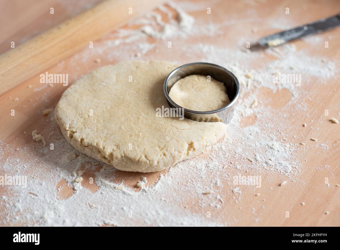 Auf die Arbeitsplatte gerollte Konusmischung mit kreisförmigem Utensil zum Zuschneiden der Form vor dem Backen im Ofen. Stockfoto
