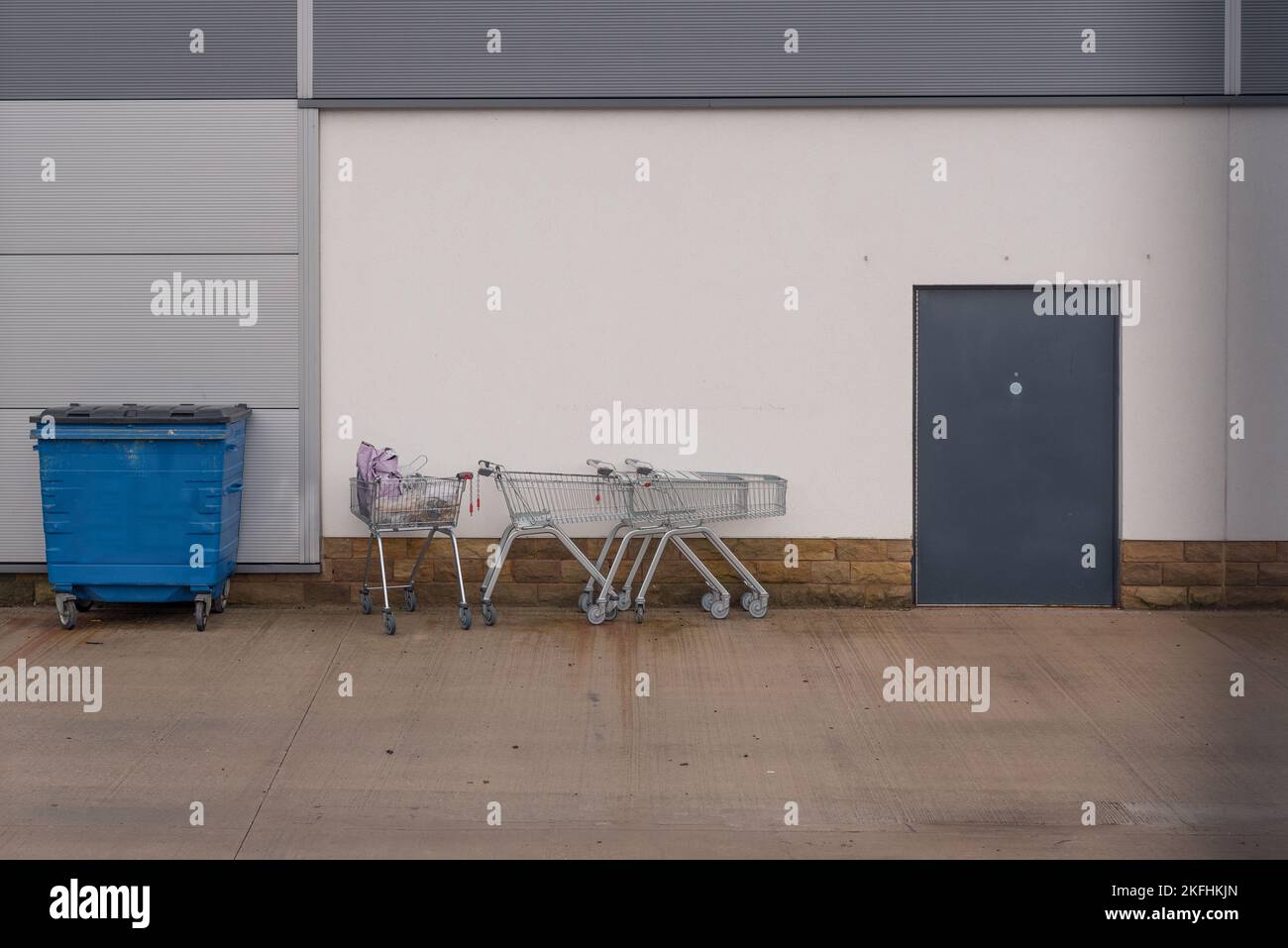 Einkaufswagen liegen hinter dem Einkaufszentrum. Blauer Industrieabfallbehälter Stockfoto