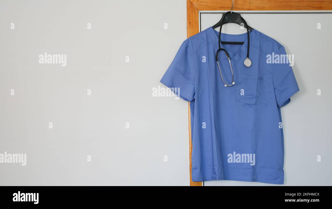 Aufgehängtes blaues Medizinhemd mit Stethoskop auf weißem Wandkopierraum Stockfoto