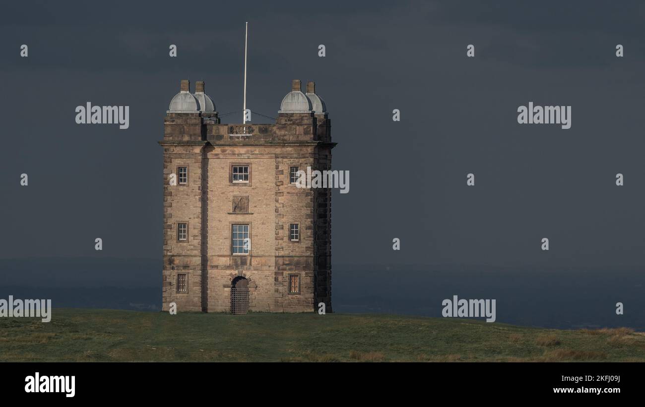 Der Käfig im Lyme Park. Sonnenlicht erhellt die Fassade mit einem dramatischen dunklen stimmungsvollen Hintergrund und Himmel. Aufgenommen in Lyme Park Cheshire UK Stockfoto