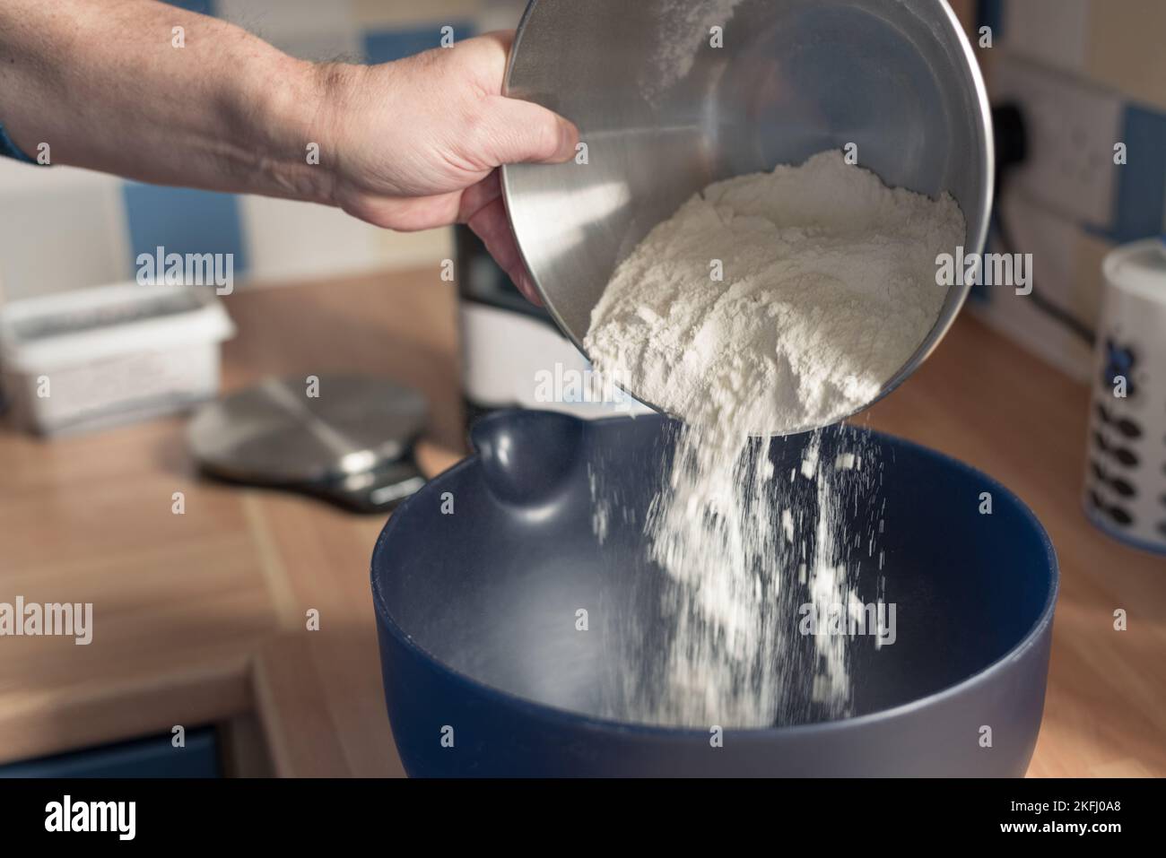 Mann, der Mehl in eine blaue Rührschüssel gießt. Stockfoto