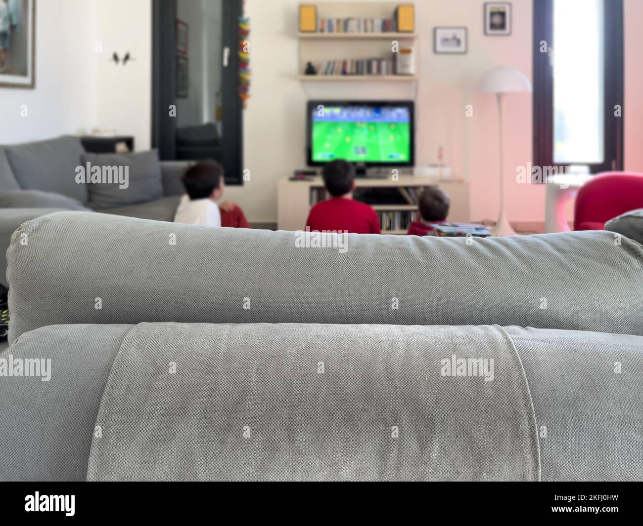 Nahaufnahme der Kopfstütze des Sofas und Geschwister, die im Wohnzimmer im Hintergrund ein Match über den Fernseher beobachten Stockfoto